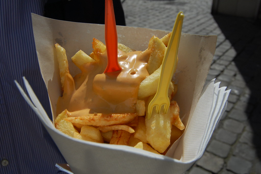 Belgian frites — thick-cut twice-fried chips served in a paper cone with a generous dollop of dipping sauce and a plastic fork