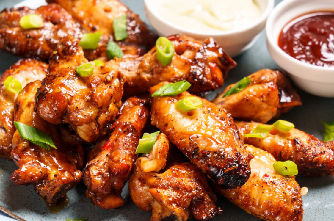Buffalo wings — crispy glazed chicken wings piled on a plate, garnished with sliced spring onion, served with dipping sauce