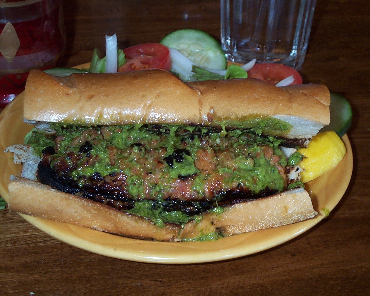 Choripán — grilled chorizo sausage in a crusty bread roll, topped with vibrant green chimichurri sauce