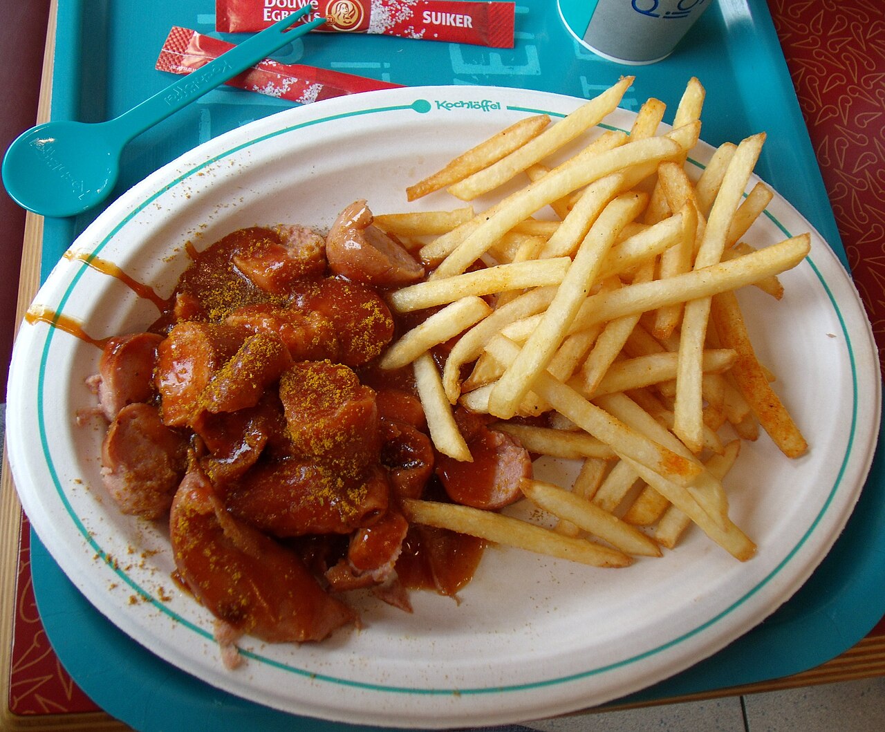 Currywurst — bratwurst slices smothered in curry-spiced tomato sauce, served alongside thick-cut fries on a round plate