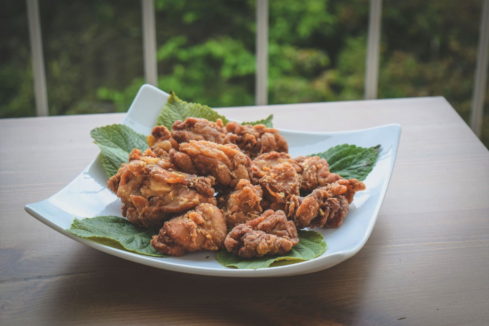 Karaage — Japanese fried chicken, golden and crispy, arranged on a bed of fresh green shiso leaves on a white plate