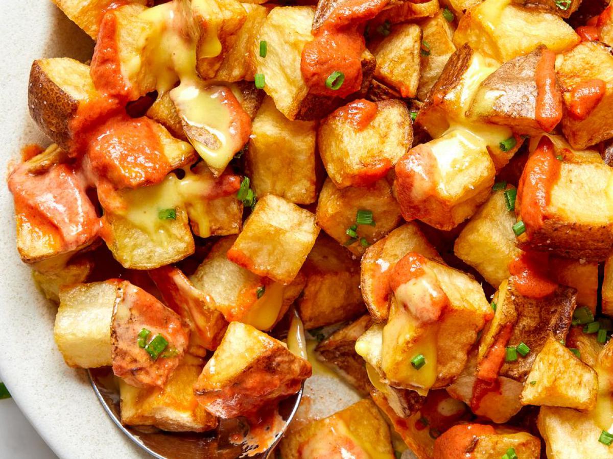 Patatas bravas — crispy roasted potato cubes drizzled with spicy red brava sauce and golden aioli, garnished with chives