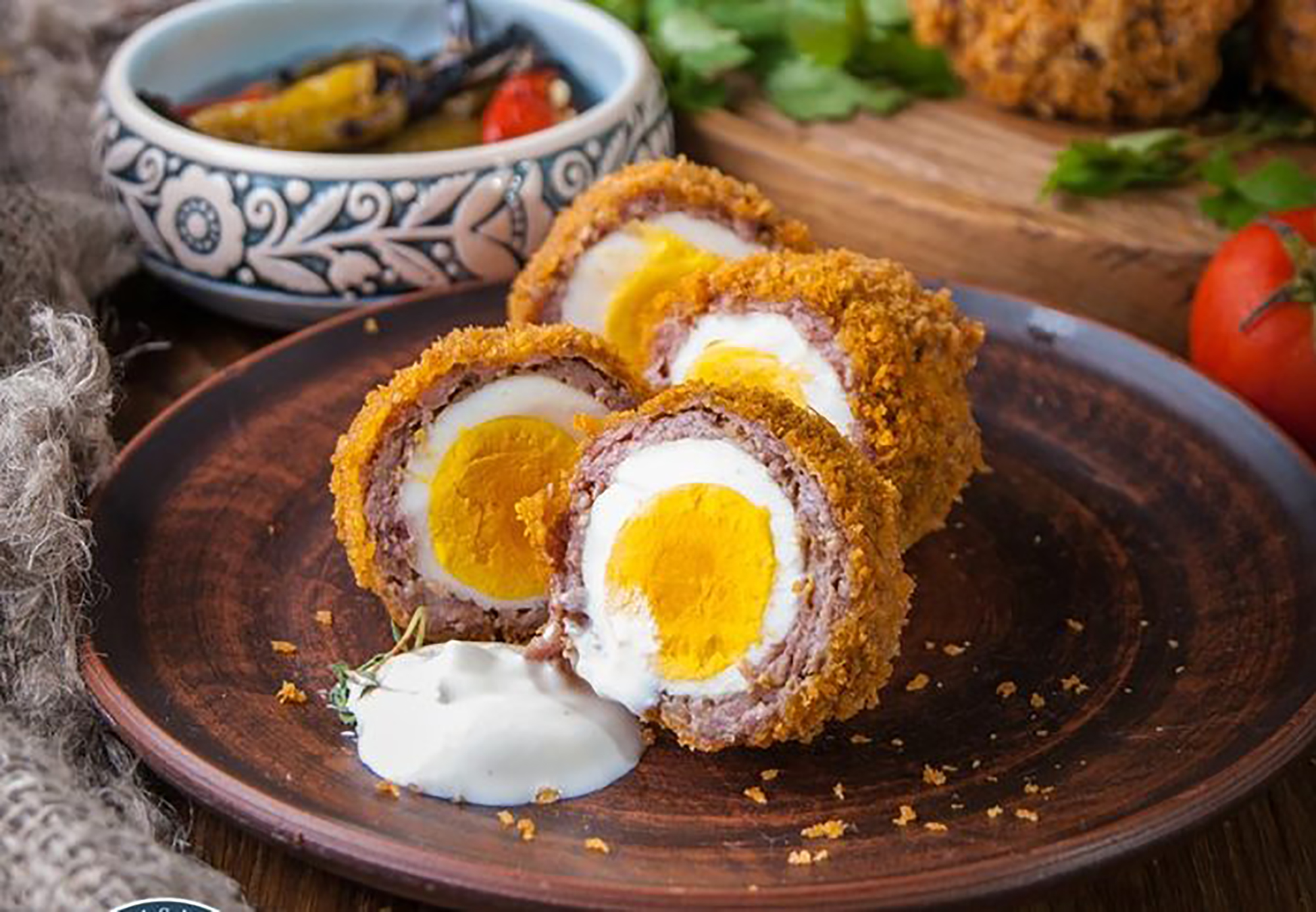 Scotch eggs — halved to reveal a soft-boiled egg wrapped in seasoned sausage meat and golden breadcrumbs, served with a white dipping sauce